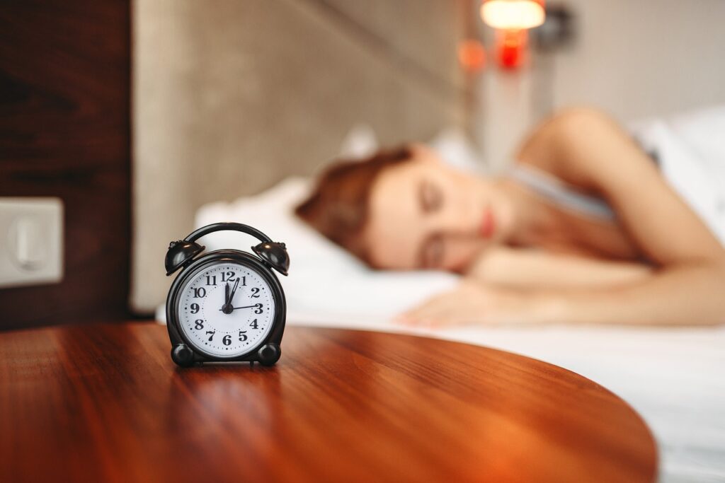 Woman sleeping in bed with an alarm clock facing the camera