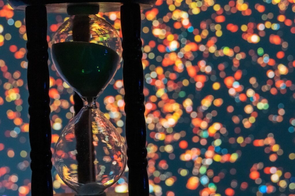 Hourglass showing the sand running through with colourful lights in the background